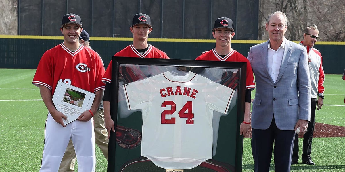 Jim Crane with three Mules players, holding the framed CRANE 24 jersey and a plaque at Crane Stadium